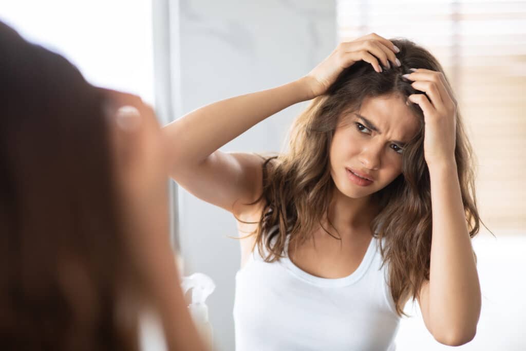 A young woman checking her hair for lice in front of a mirror.