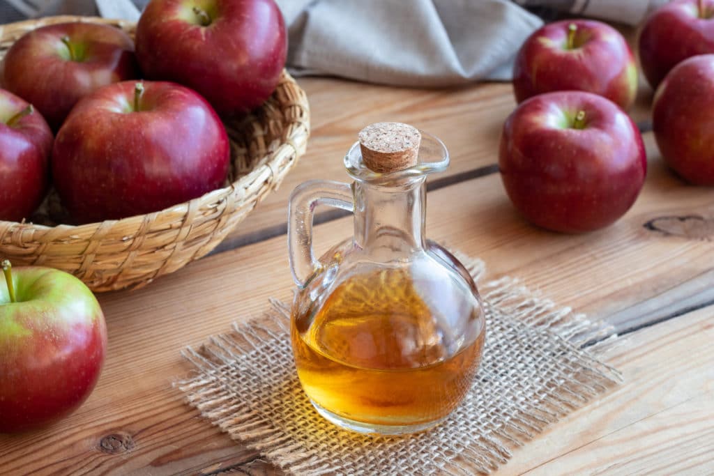 A bottle of apple cider vinegar with apples around.