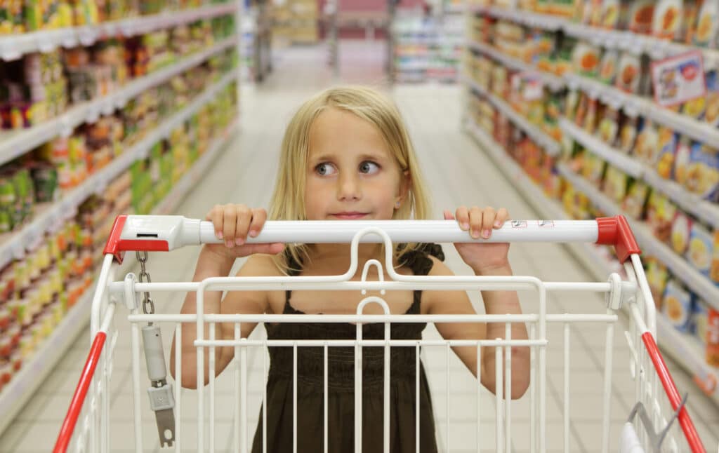 A young girl pushing a trolley in the supermarket aisle.