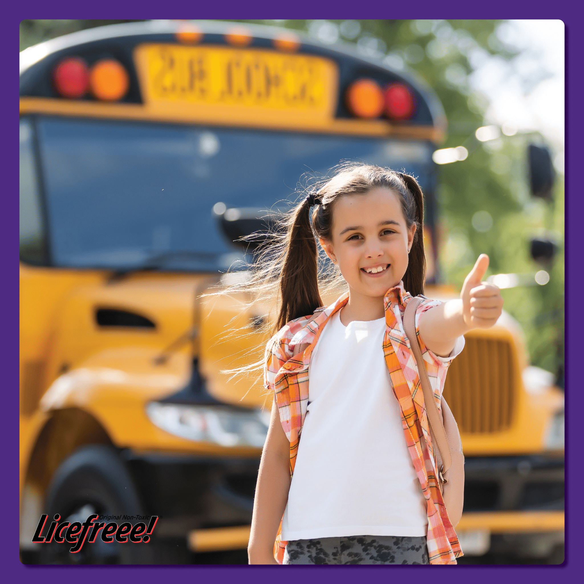 A young girl with two ponytails is showing a thumbs-up in front of a school bus.