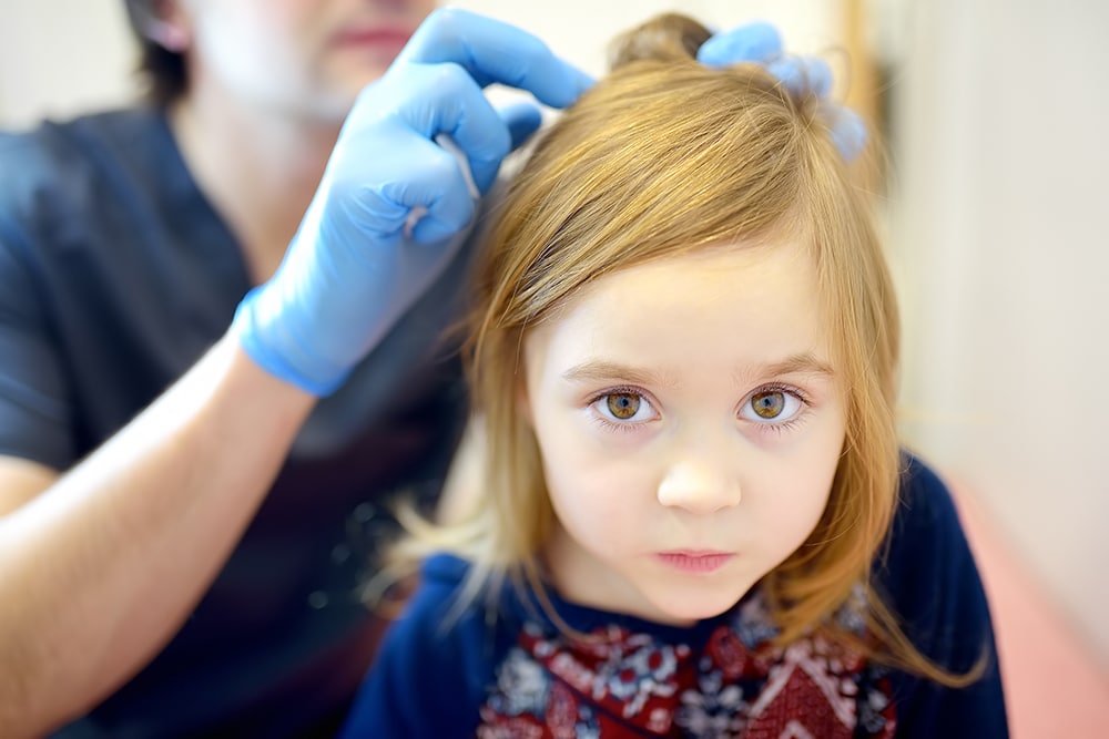 The little girl with a serious face is being checked by a nurse for head lice.